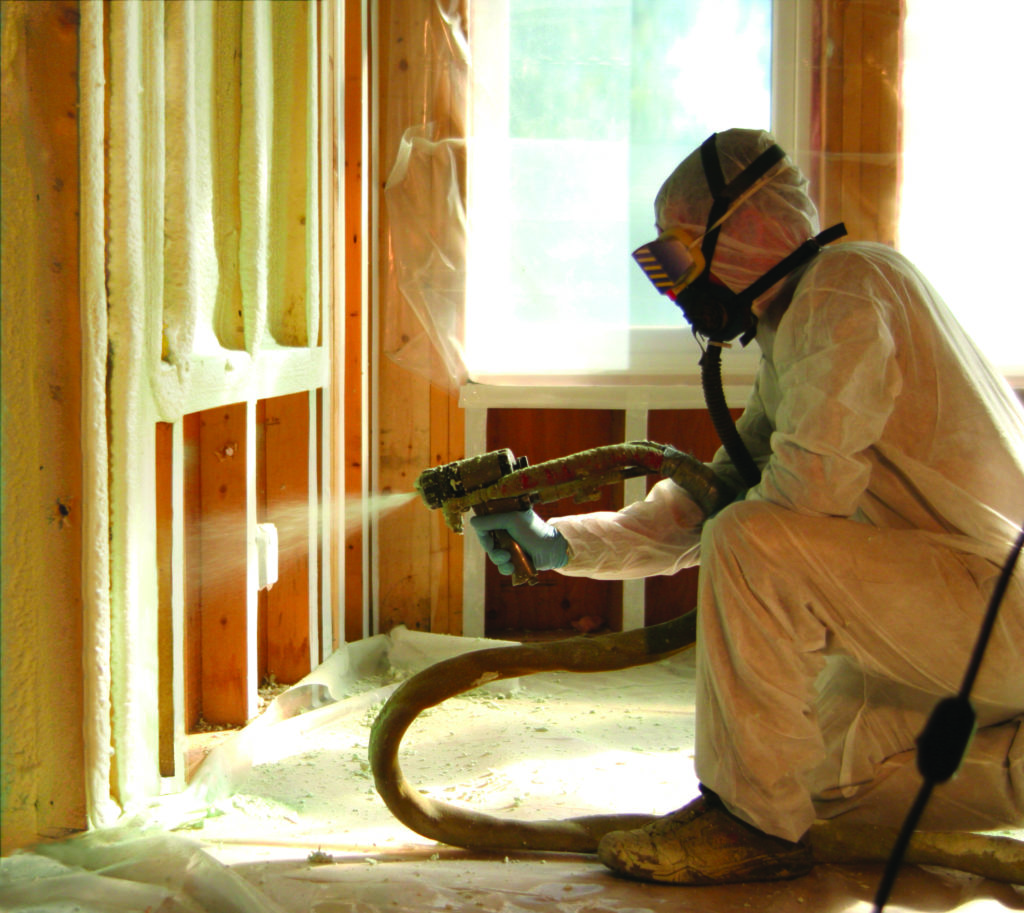 A technician in PPE installing spray foam insulation in a home's walls